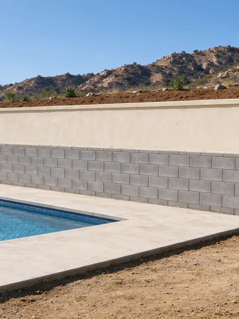 Block retaining wall with a stucco-finished upper face holding the slope beside a backyard pool on an El Cajon lot