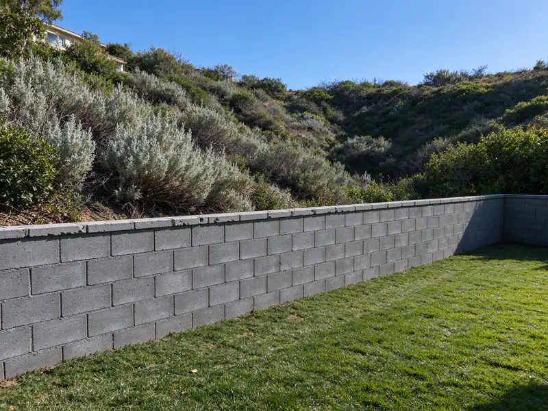 Canyon-edge backyard with a gray concrete block retaining wall and native brush beyond it