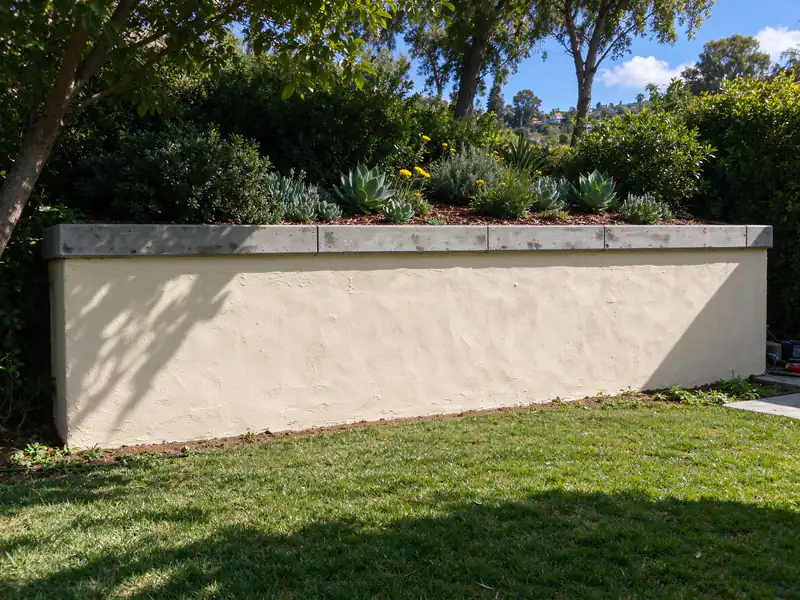 Finished block retaining wall with a smooth stucco face and a precast cap along a sloped San Diego yard