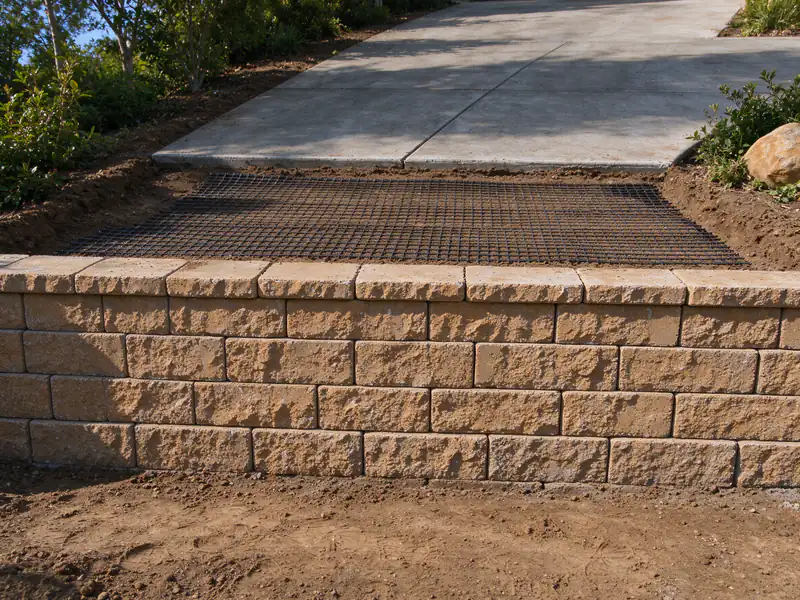 Geogrid layer laid over compacted fill behind a segmental block wall below a driveway