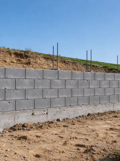 Gray concrete block retaining wall under construction in San Diego, with vertical rebar rising from open block cells above a poured concrete footing