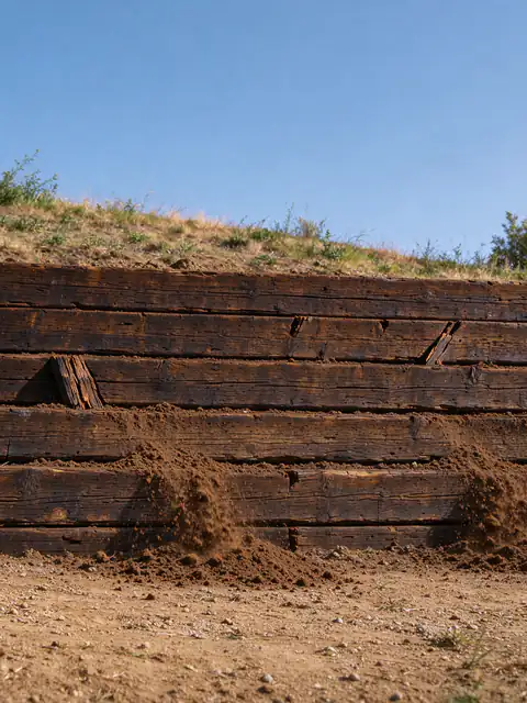 Railroad tie retaining wall leaning outward along a backyard slope, with dark, split ends and soil spilling between the lower ties
