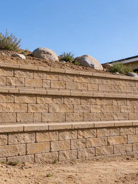 Tan segmental block retaining wall stepping up a decomposed granite slope with granite boulders above it in Escondido